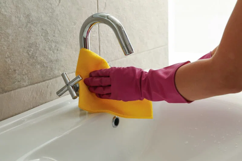 Gloved hand cleaning a bathroom tap